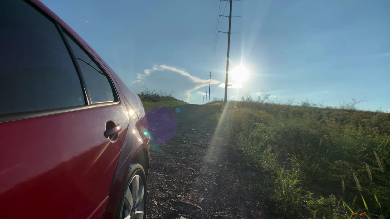 coche rojo bajando una colina con el sol detrás