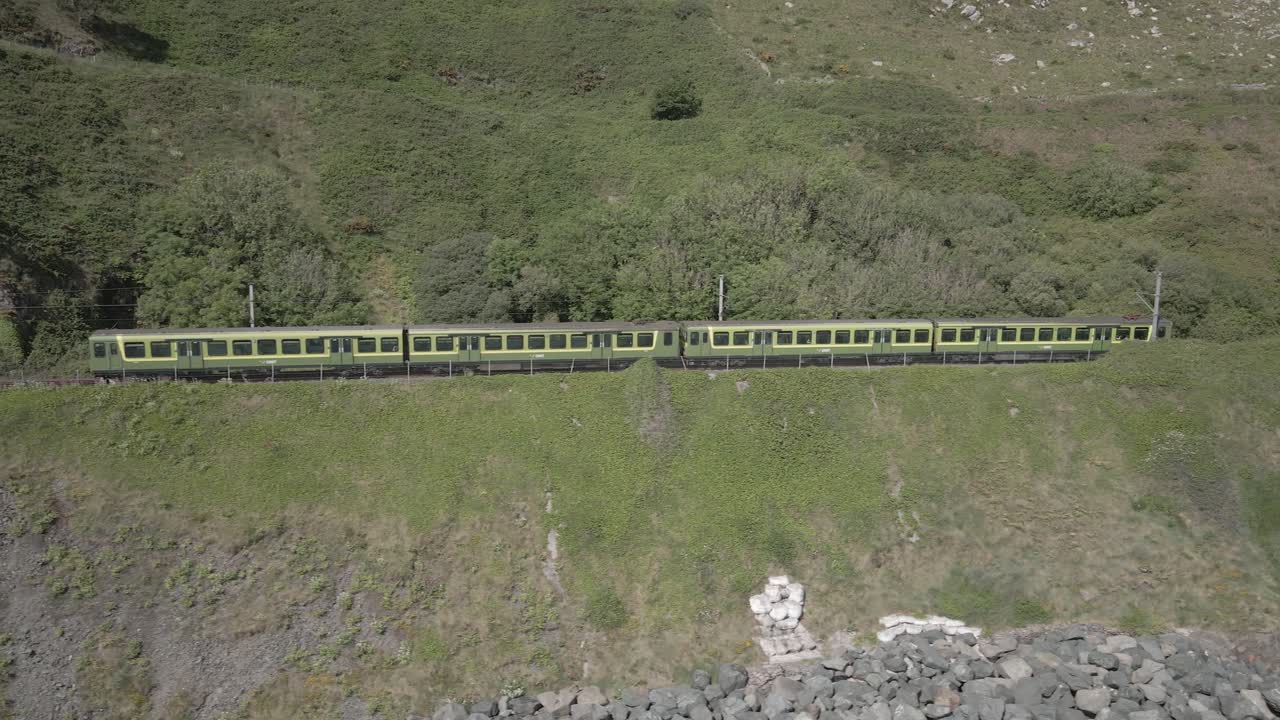 tren saliendo del túnel en la montaña de bray head en el condado de wicklow, irlanda en un día soleado
