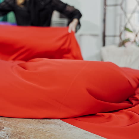seamstress laying out beautiful red cloth on a wooden table. work place table of tailor in workshop and a big piece of red fabric indoors.