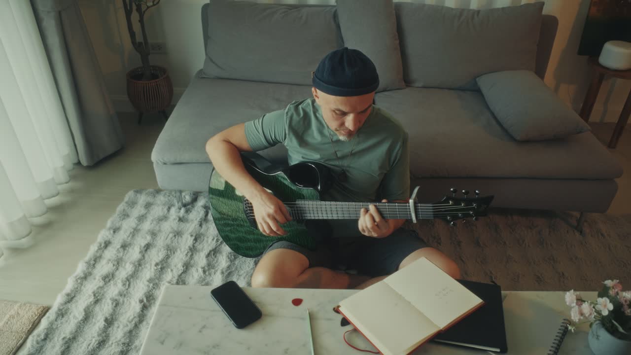 Mann som spiller akustisk gitar og skriver musikk hjemme.