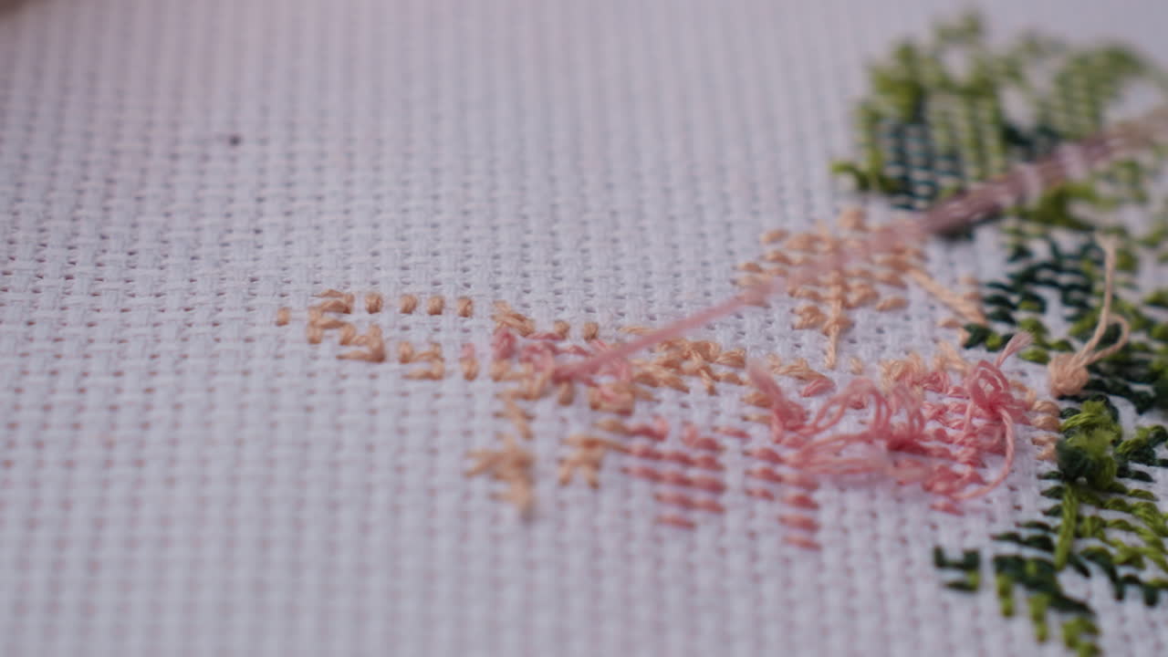 Close up craft person cutting thread on embroidered fabric using small scissors, showing delicate precision, texture of cross stitched pattern, gentle hand finishing handmade artwork with care