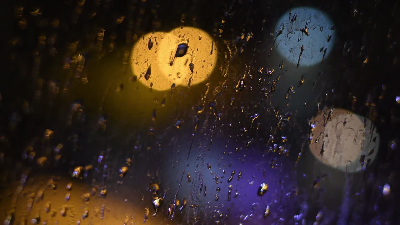gotas de lluvia nocturna en la ventana sucia con luces bokeh en el fondo