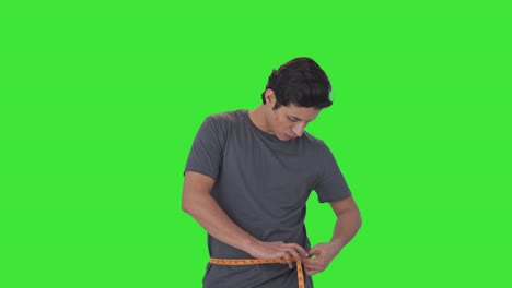 Upset-Indian-man-measuring-waist-using-inch-tape-Green-screen