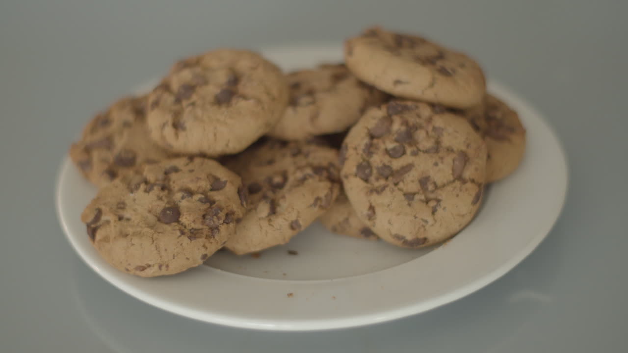 Hand grabbing chocolate chip cookies from a white plate - high angle