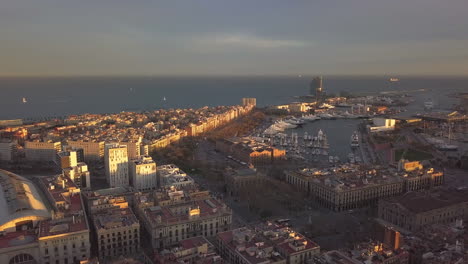 Erstaunliche-Panoramaaufnahmen-Aus-Der-Luft-Des-Städtischen-Küstenbezirks-Und-Des-Jachthafens-Bei-Sonnenuntergang.-Gebäude,-Die-Vor-Sonnenuntergang-Von-Heller-Sonne-Beleuchtet-Werden.-Barcelona,-Spanien