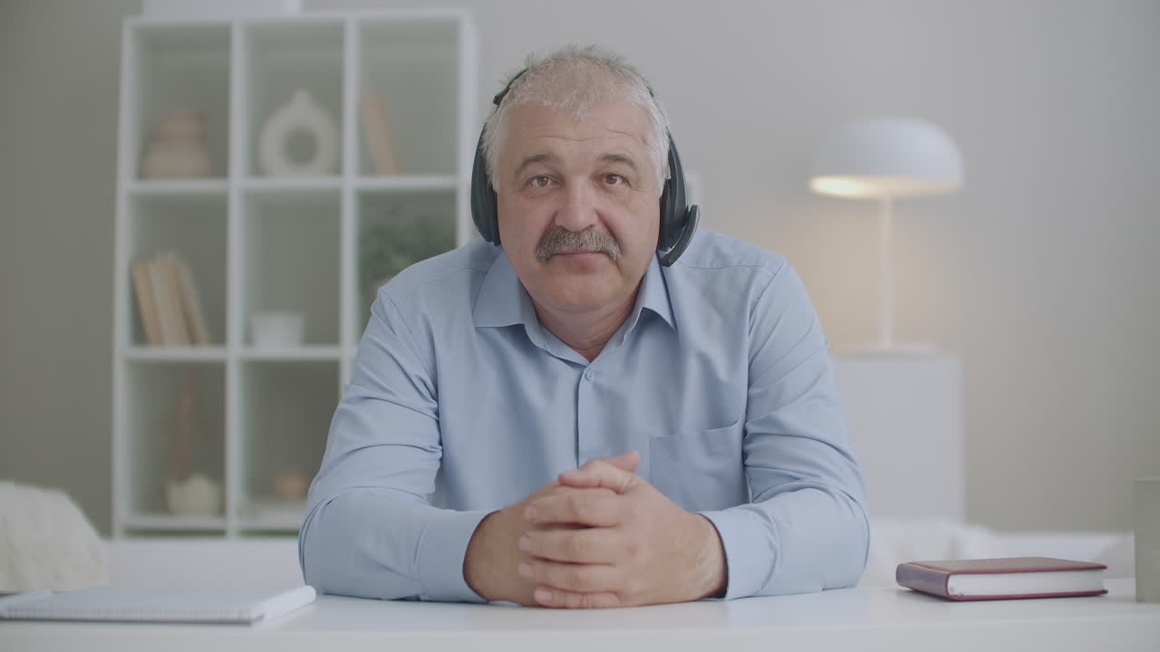 hombre de mediana edad con auriculares en la cabeza está asintiendo con la cabeza y mirando la cámara video llamadas y concepto de chat en línea