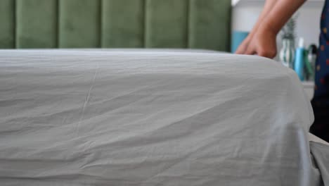 person making bed with gray sheets