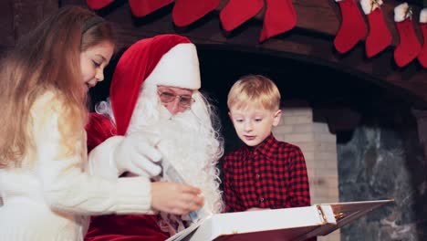 a boy and a girl are reading a book with santa claus in a room near the fireplace with christmas stockings