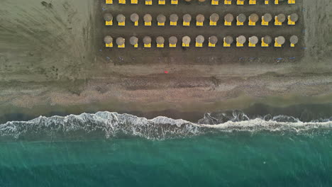 Aerial-Top-Down-View-of-Coastal-Beach-with-Yellow-Deckchairs-and-Umbrellas-in-Spain,-Malaga