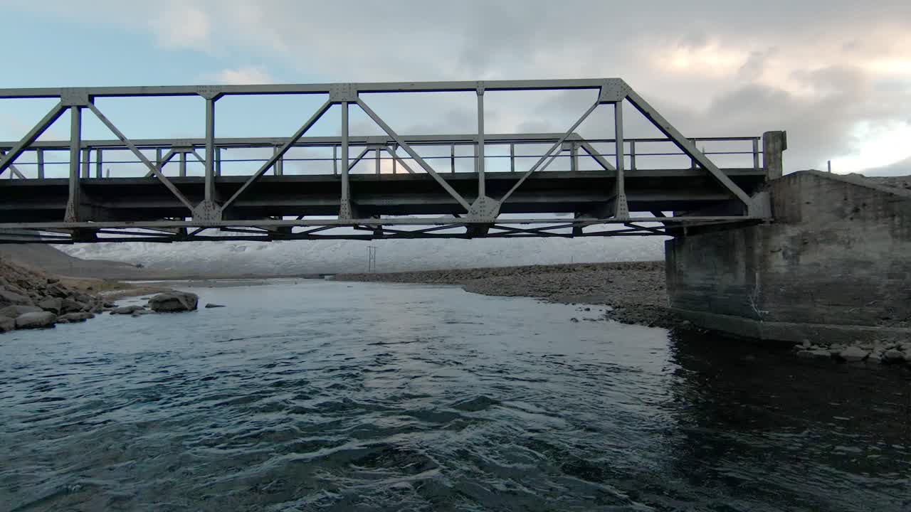 드론이 강 위와 다리  ⁇ 에서 큰 바위 산을 향해 날아가고 있습니다.