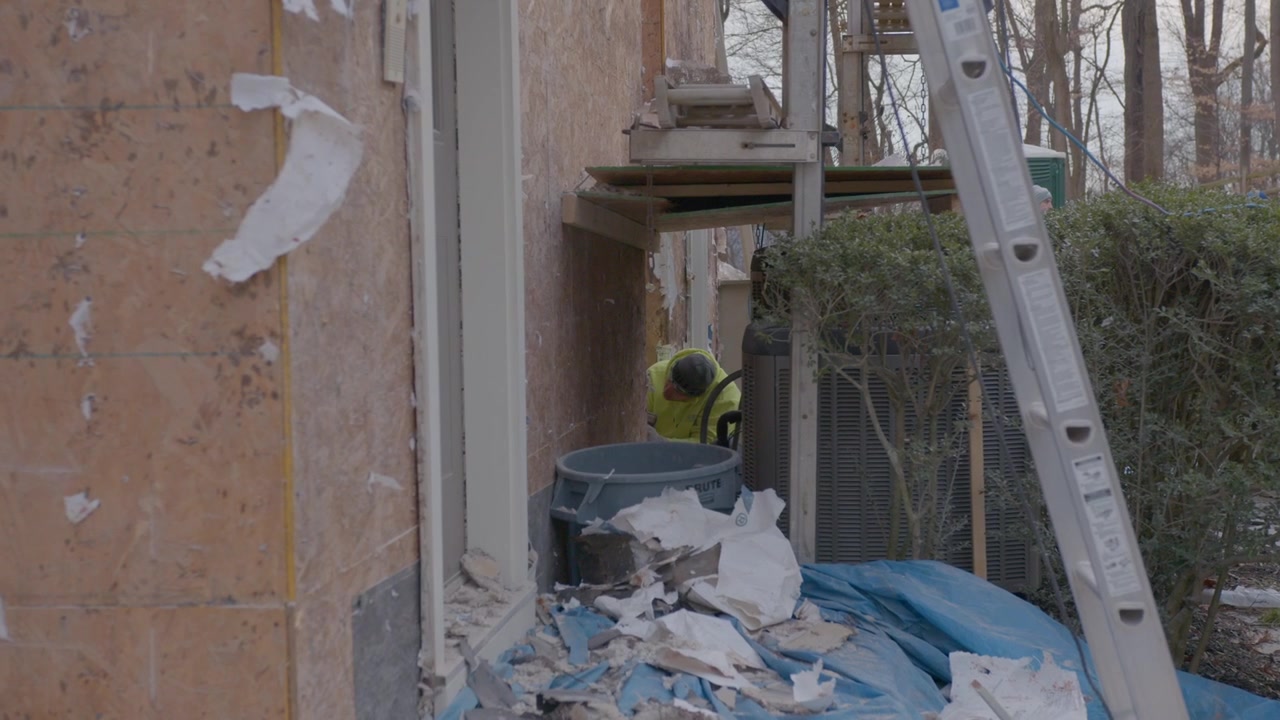 Un uomo sta rimuovendo il rivestimento da una casa sotto una scala