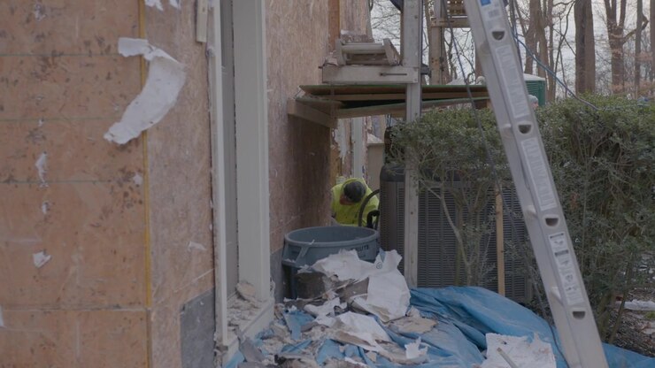 Un hombre está quitando el revestimiento de una casa debajo de una escalera.
