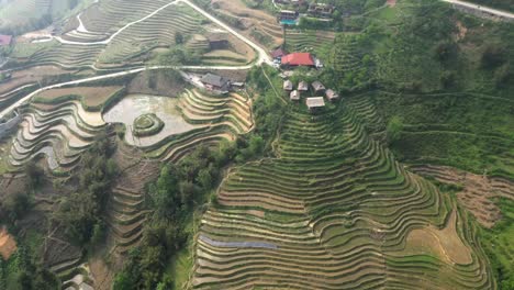 a scenic drone shot shows rice terraces layered over green hills, with village huts and a winding road, representing sustainable farming, tradition, and asian rural landscapes.