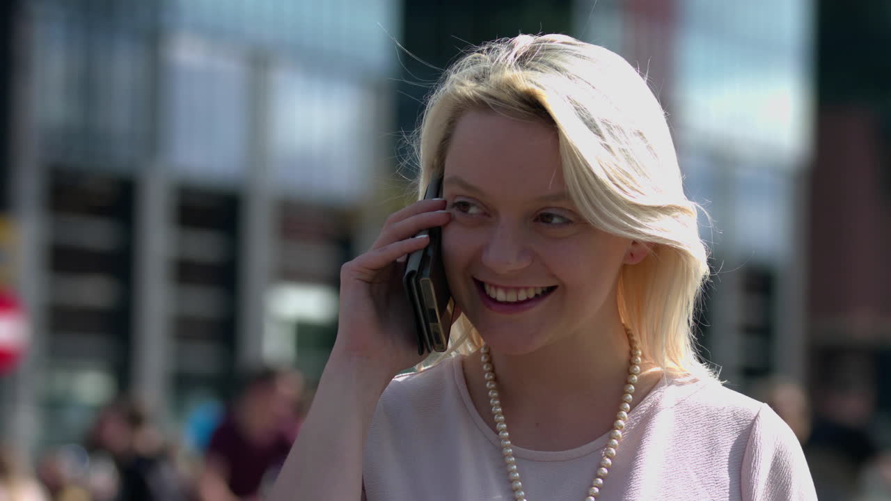 Close up of blonde woman calling using smart phone. Beautiful light hair businesswoman talking on cellular phone wearing business attire with pearl beads as accessories. Corporate female employee