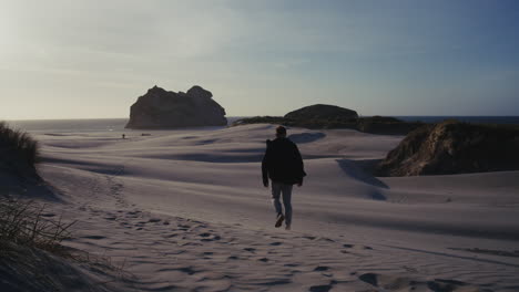man walking through sand dunes at beach