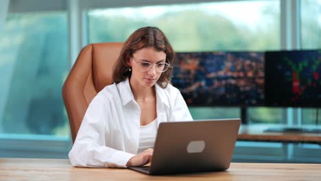 mujer de negocios trabajando en un cuaderno en una oficina moderna con fondo de vidrio y pantalla de computadora