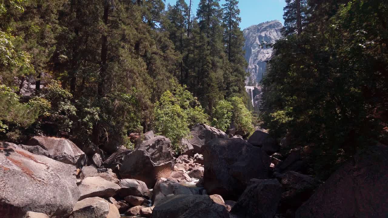 Toma lenta con cámara en mano de pilas de grandes rocas de granito en un río seco con una cascada al fondo