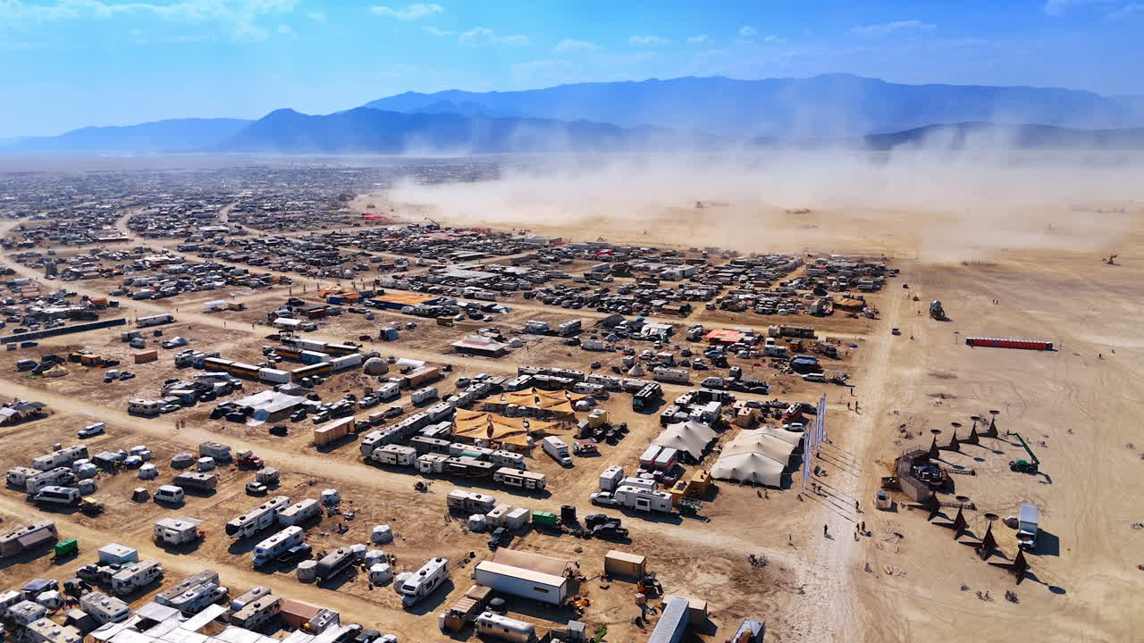 Stor campingplads organiseret i ørkenen. En støvsky rejser sig i baggrunden. Burning Man-festival i Black Rock-ørkenen