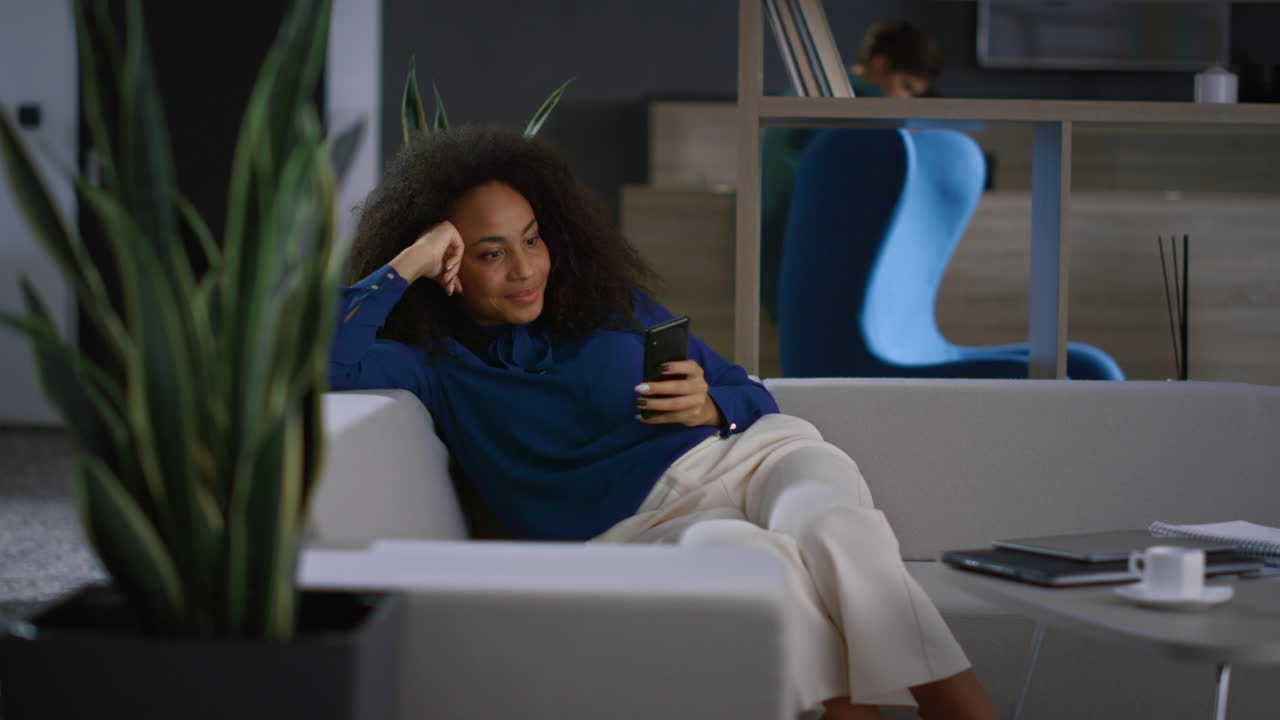 Avslappet forretningskvinne surfer på internett med mobiltelefon på et moderne kontor.