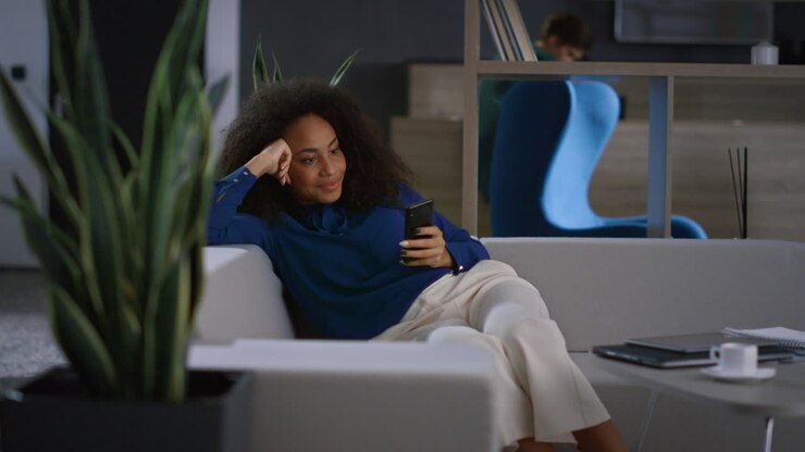 Avslappet forretningskvinne surfer på internett med mobiltelefon på et moderne kontor.