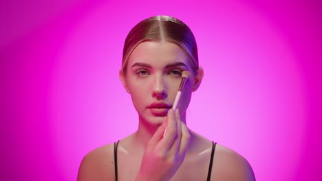 blonde caucasian girl applies powder makeup on her eyelids, close up studio shot, young model, styling and beauty