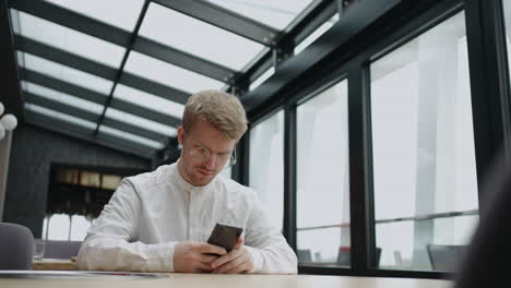 hombre adulto con teléfono inteligente en un restaurante o espacio de coworking moderno navegando por internet en un teléfono móvil