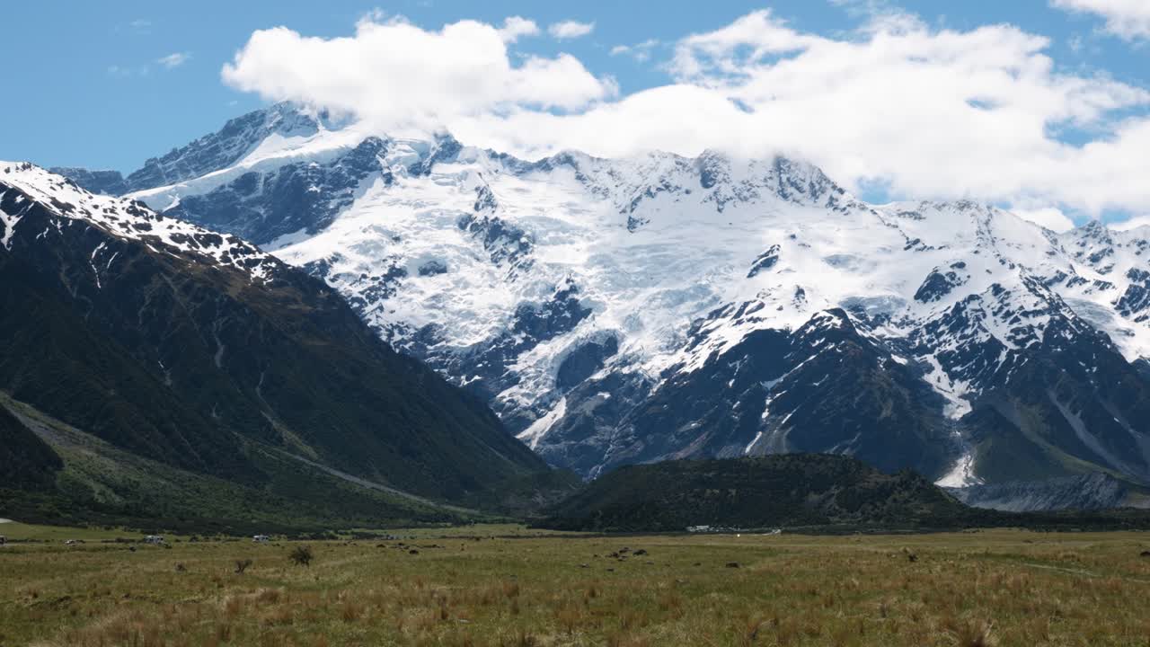 View of fields, snowy mountains, Mount Sefton, glaciers, and landscape on a clear sunny summer day in Mount Cook National Park, New Zealand.