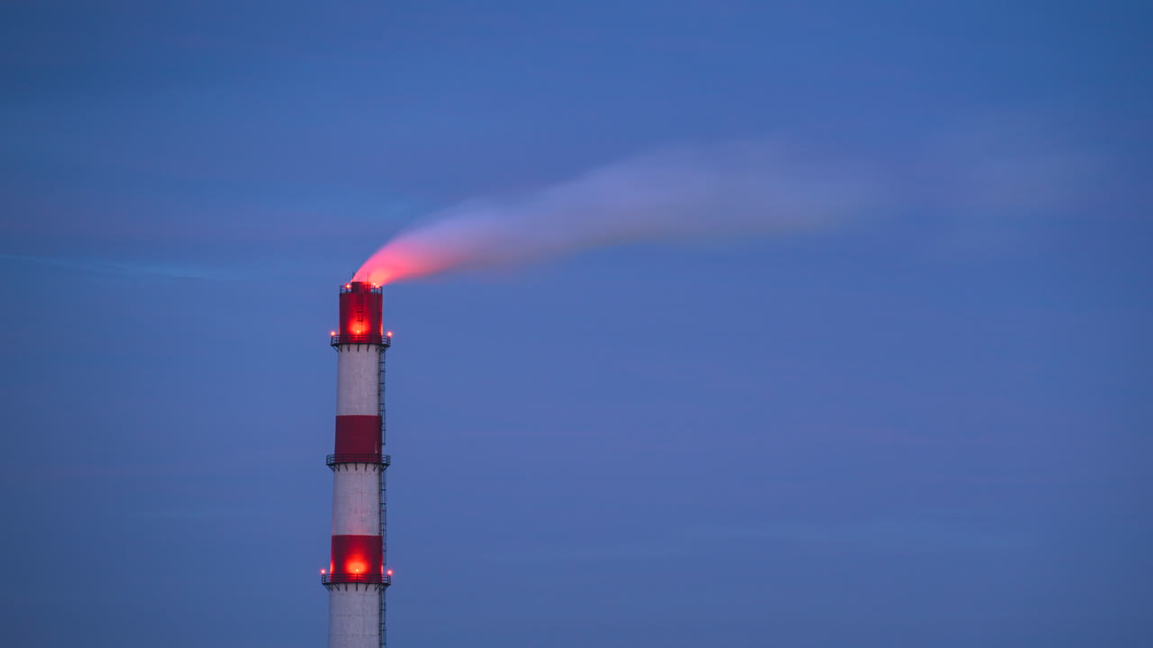 Timelapse of a red and white smokestack emitting a plume of smoke into the air with the evening sky on the background