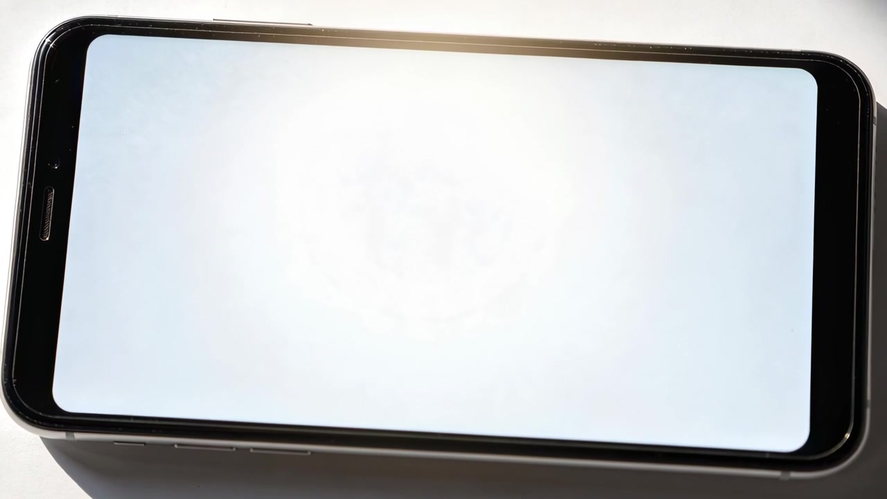 Mostrando uno smartphone con cornice nera che riflette luce in movimento su un tavolo bianco, con un bagliore circolare che si espande.