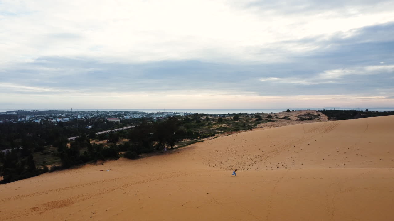 자연 환경에서 삶과 행복을 축하하는 파란색 물결 모양의 드레스를 입고 사막 모래 언덕에서 혼자 달리는 젊은 여성의 공중