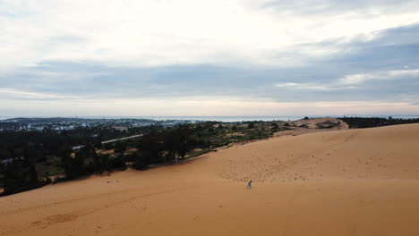 Aerial-of-Young-woman-running-alone-on-desert-sand-dunes-with-blue-wavy-dress-celebrating-life-and-happiness-in-natural-environment