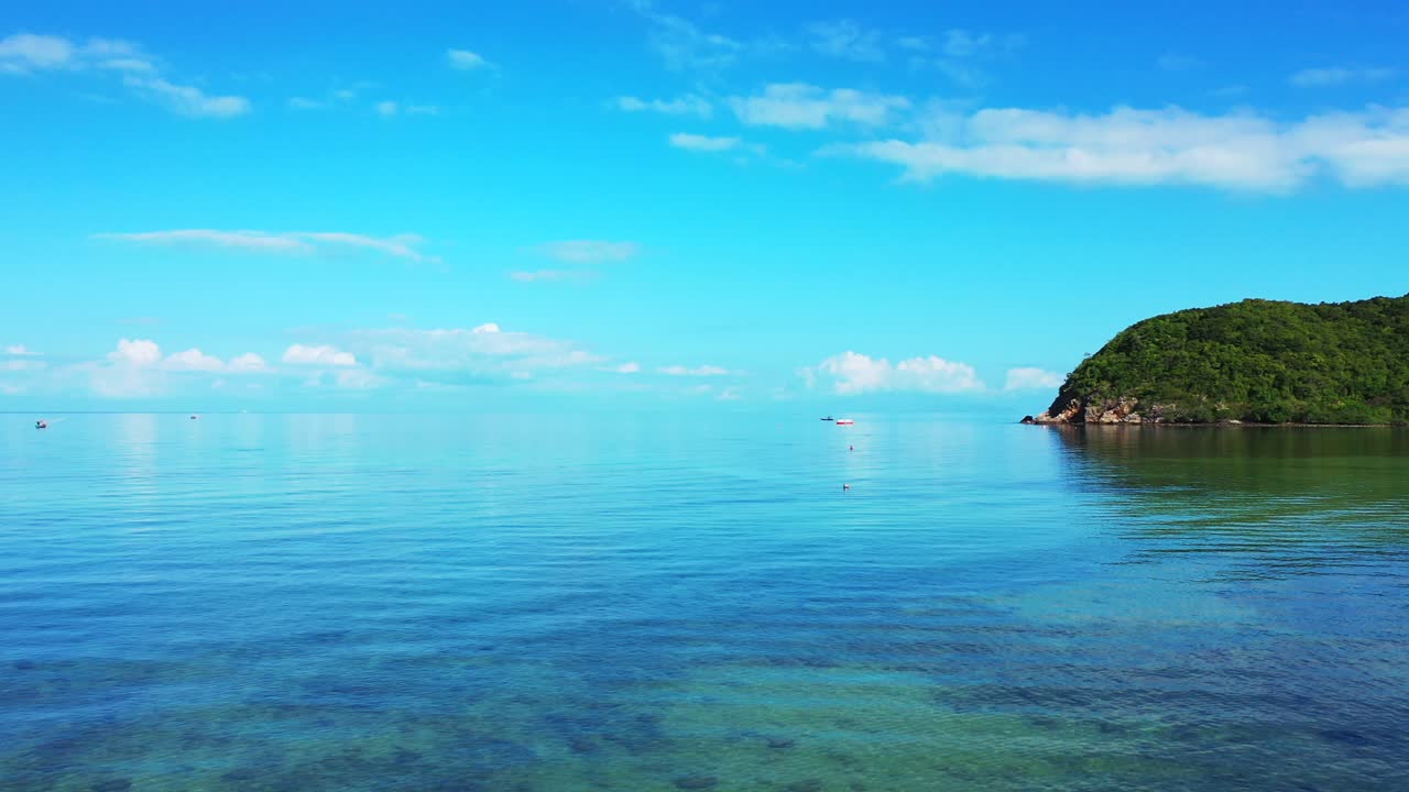 Shallow lagoon with corals on seabed under calm clear water reflecting white clouds on blue sky and tropical island cape in Thailand