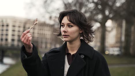 young woman in a black coat standing in a park in autumn in afternoon and watch a leaf in the wind