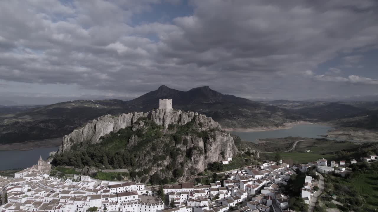 4K drone shot of Zahara de la Sierra, Spain, filmed with a DJI at 30fps. A cinematic backward flight revealing the medieval castle, the stunning reservoir, and the village below.