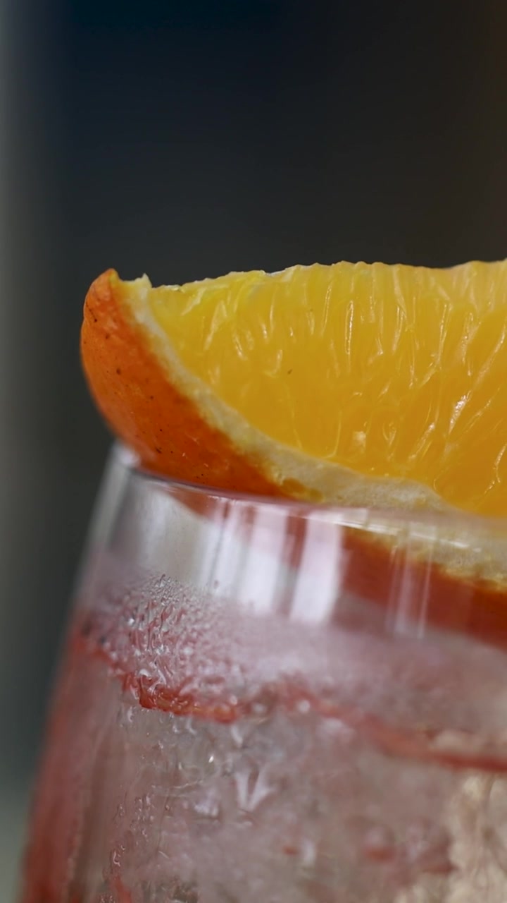 Primo piano di un Aperol Spritz ghiacciato guarnito con una fetta d'arancia, che evidenzia la condensa e i colori vivaci.