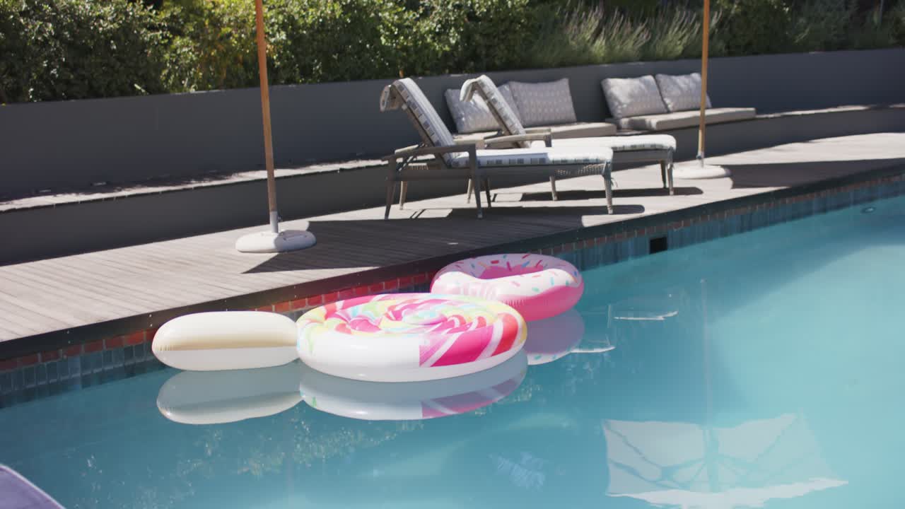 Camera is shifting downward and pool floats are drifting closer, highlighting towel, hat on deck