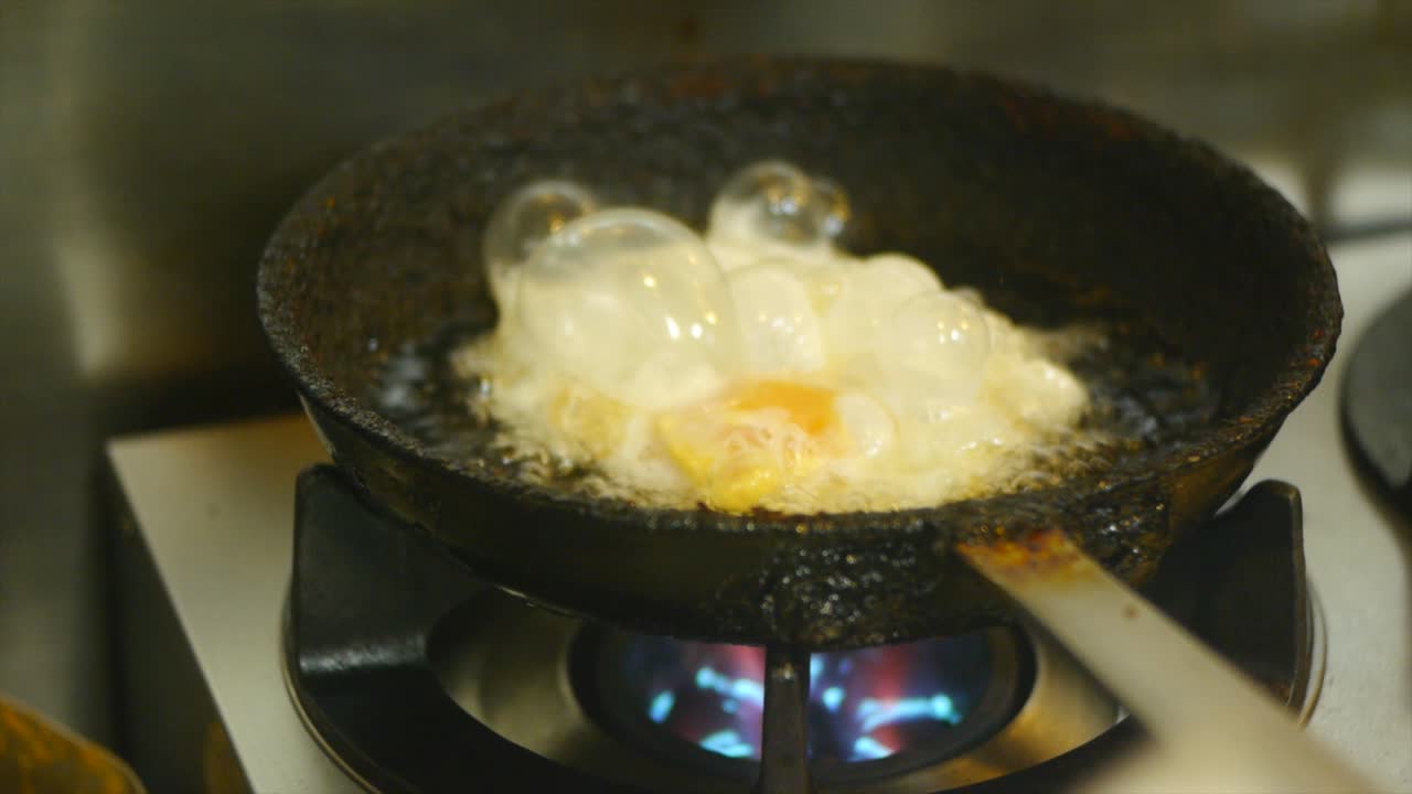 Egg being oil fried and flipped in frying pan on gas fire stove filmed in close up