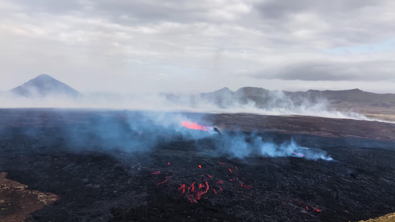 Lava flows at Fagradalsfjall, smoky scene with mountains in backdrop, daylight