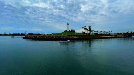 Wide-angle-shot-of-a-boat-crossing-in-front-of-the-light-house-in-the-harbor-of-Long-Beach-California