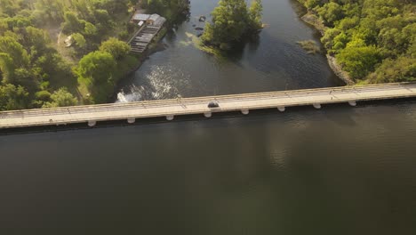 aerial tracking shot of black car driving on bridge dam over river during sunset in argentina - car journey in wilderness of south america in 4k