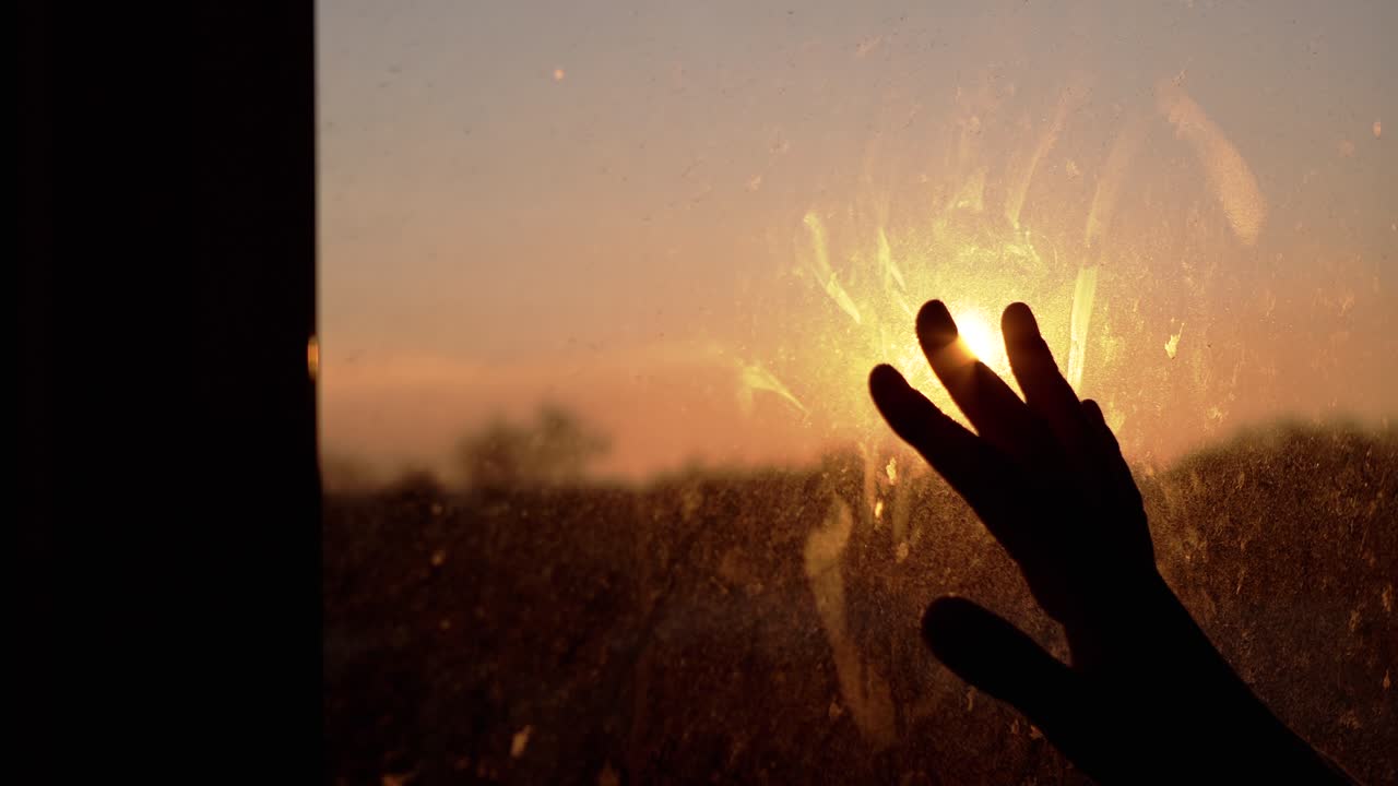 mano femenina estirando para el sol por la ventana, tocando el vidrio sucio en la habitación