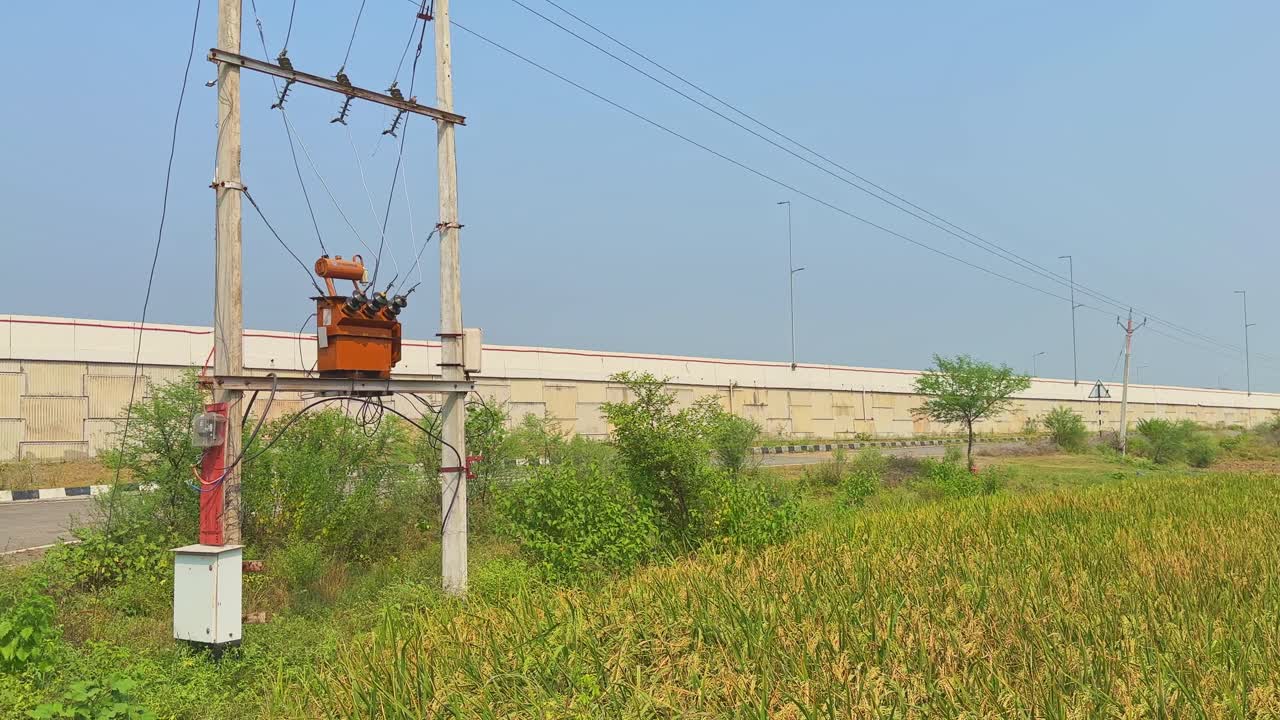 A panning shot that stops at a small electric transformer installed near farmland, used to supply electricity to farmers for irrigation and other uses