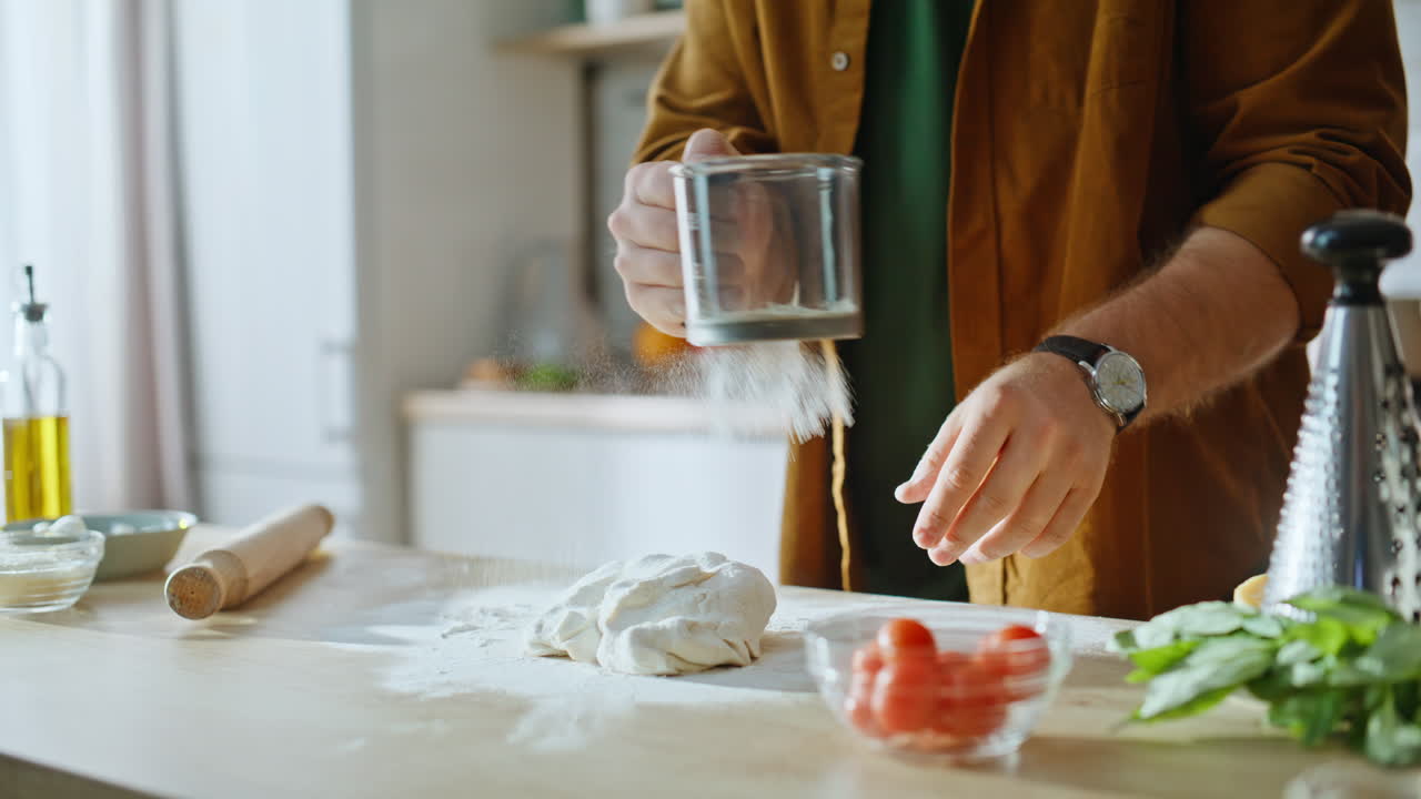 Baker hands adding flour to homemade dough at wooden kitchen counter closeup