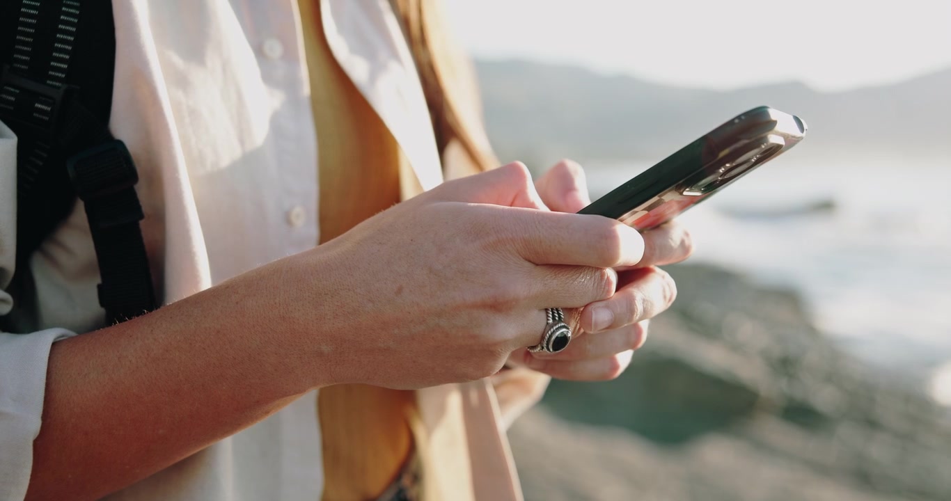 Donna che Usa lo Smartphone all'Aperto vicino all'Oceano al Tramonto