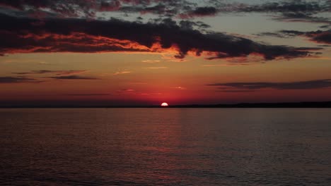in maldonado, uruguay, the last piece of sun disappears over the horizon. beautiful colors fill the sky, with glowing clouds and soft reflections over the calm water at sunset