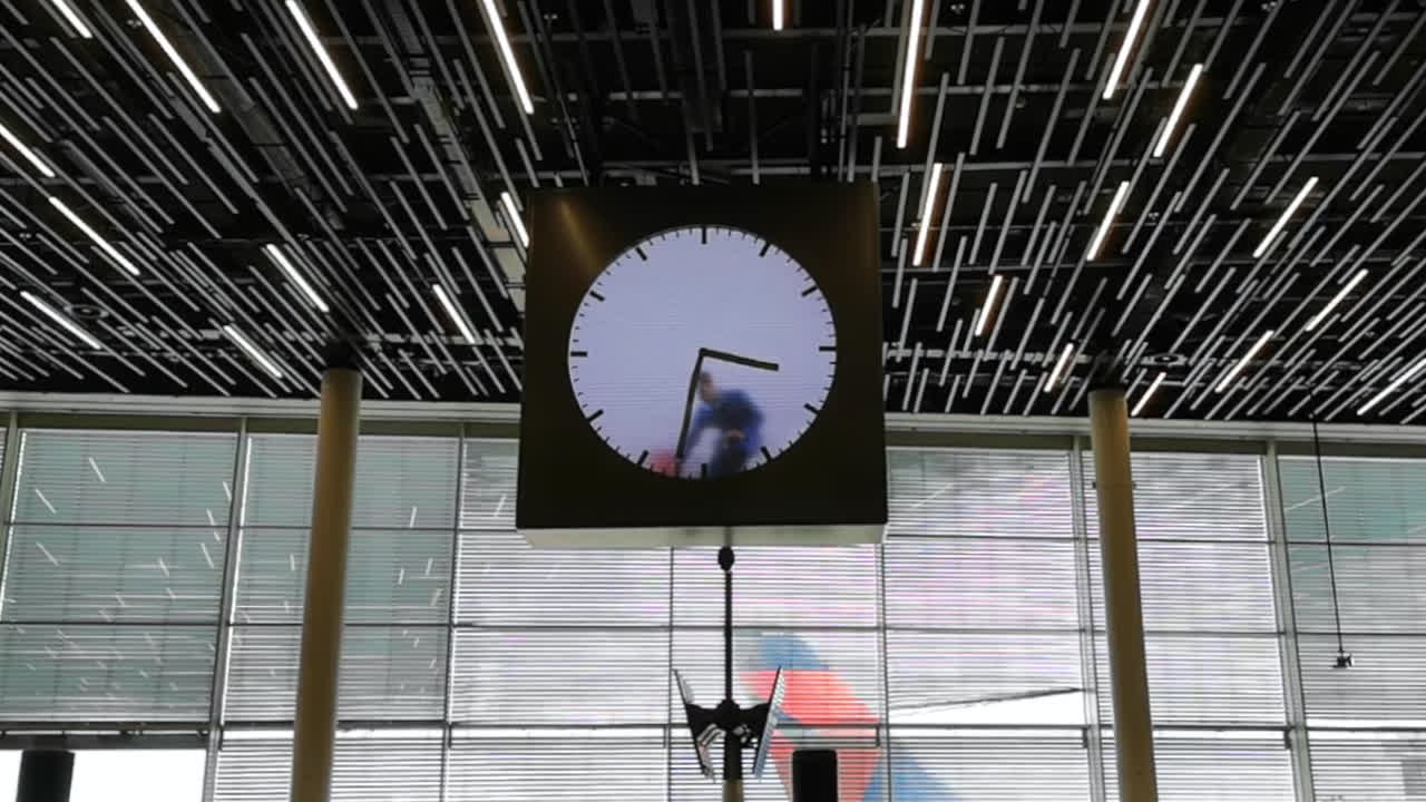 Amsterdam Airport lounge, huge clock being cleaned by man in blue overcoat.
