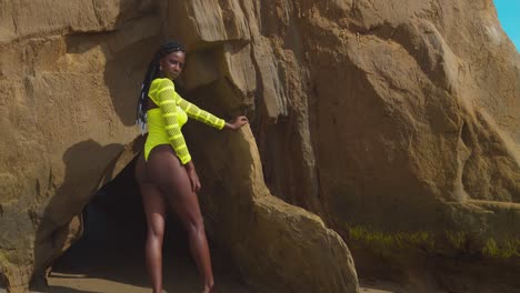 pretty african queen stands at the entrance to a cave in a yellow sexy bikini