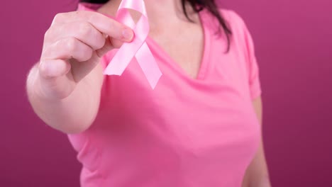 Video-De-La-Sección-Media-De-Una-Mujer-Caucásica-Sosteniendo-Una-Cinta-Rosa-De-Concientización-Sobre-El-Cáncer,-Con-Fondo-Rosa