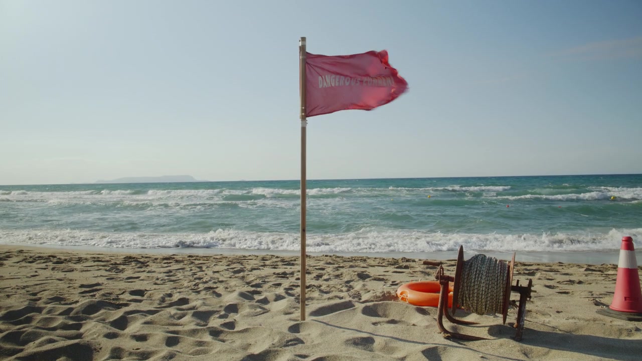Una bandiera rossa di avvertimento sventola nel vento forte su una spiaggia sabbiosa, segnalando pericolo a causa di onde e correnti marine agitate