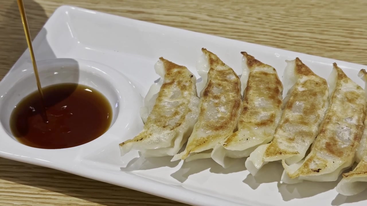 Close-up of golden fried gyoza served with savory dipping sauce, showcasing a crispy wrapper and juicy filling in an appetizing Japanese-style appetizer.